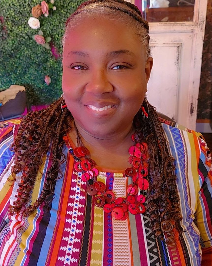 68110c6061a02_Keena Richard (1) A woman with long braids wearing colorful clothing.